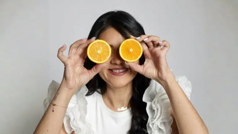 Mujer sonriendo y sosteniendo medias naranjas delante de sus ojos