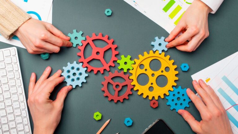 Manos posicionando engranajes de varios colores en una mesa, generando un sistema conectado